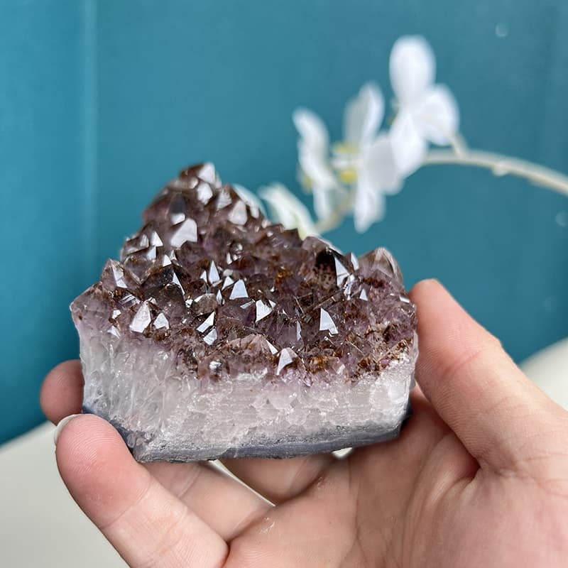 Amethyst crystal cluster displayed with white orchids on table