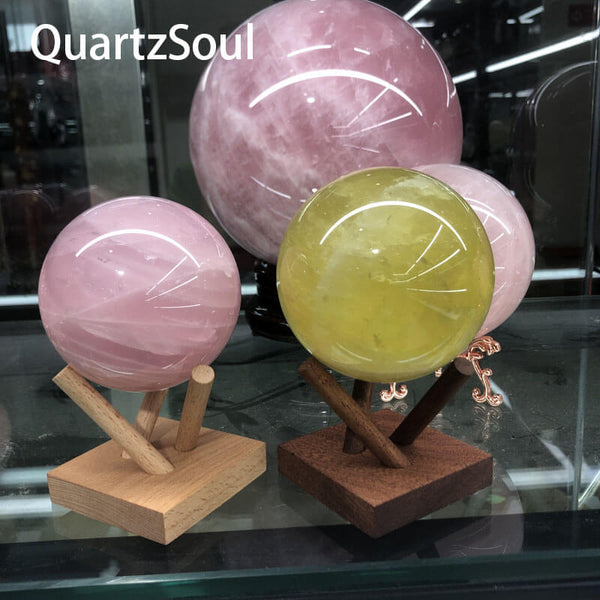 Rose quartz and citrine crystal spheres showcased on light and dark wooden display stands