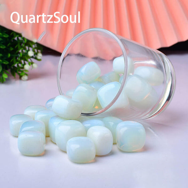 Premium Opal tumbled stones spilling from glass container with pink background
