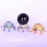 Black crystal sphere displayed on decorative silver stand with beaded legs