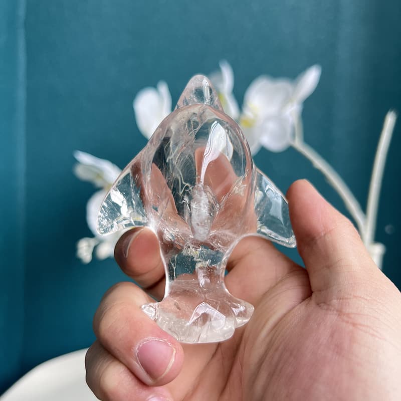 Hand holding clear quartz dolphin carving to demonstrate size and transparency