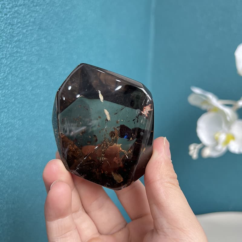 Hand holding natural smoky quartz free form showing size and ergonomic shape