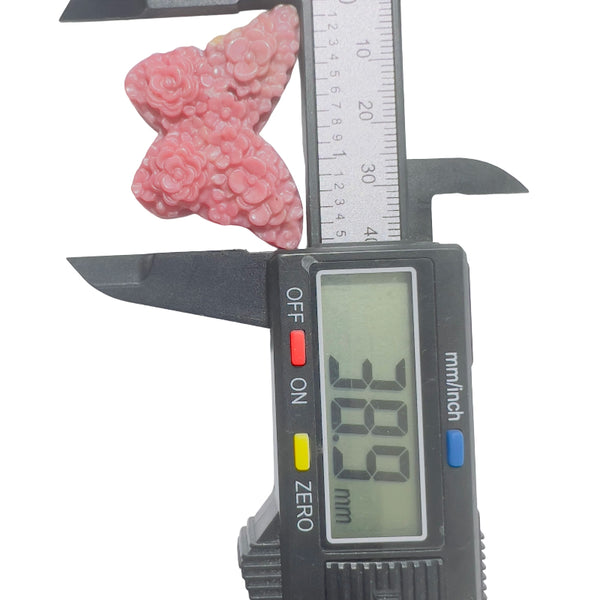 Pink rhodonite butterfly crystal carving displayed on decorative stand